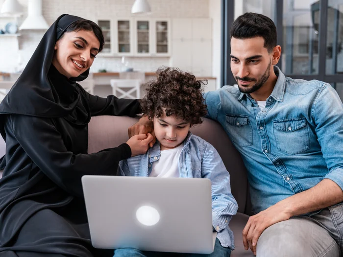 صورة توضيحية لأسرة تساند طفلًا يتعلم عبر حاسوب محمول في المنزل